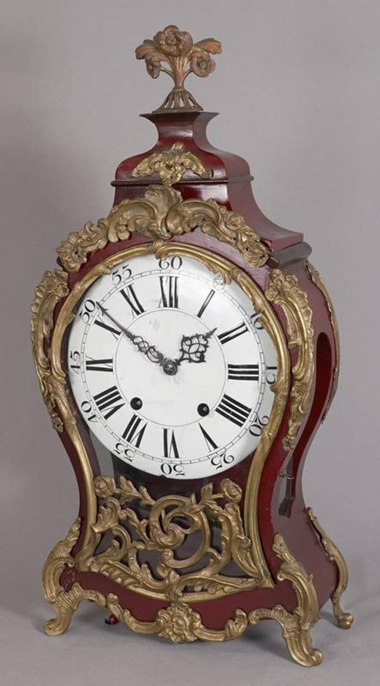 A baroque-style bracket clock in a reddish-finished, waisted case with brass acanthus-leaf ornamentation and a console base.