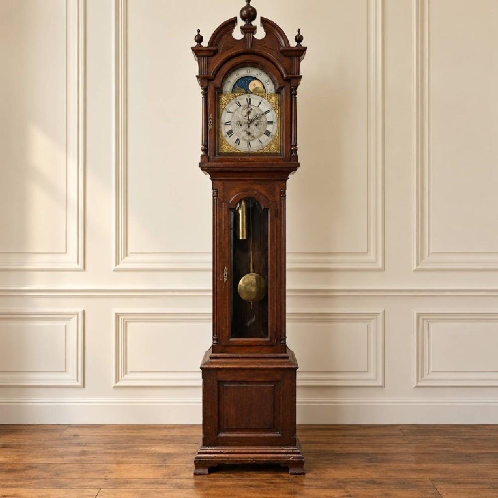 Full view of the tall wood grandfather clock showing the broken arch pediment, glass-front door, and moon phase dial.