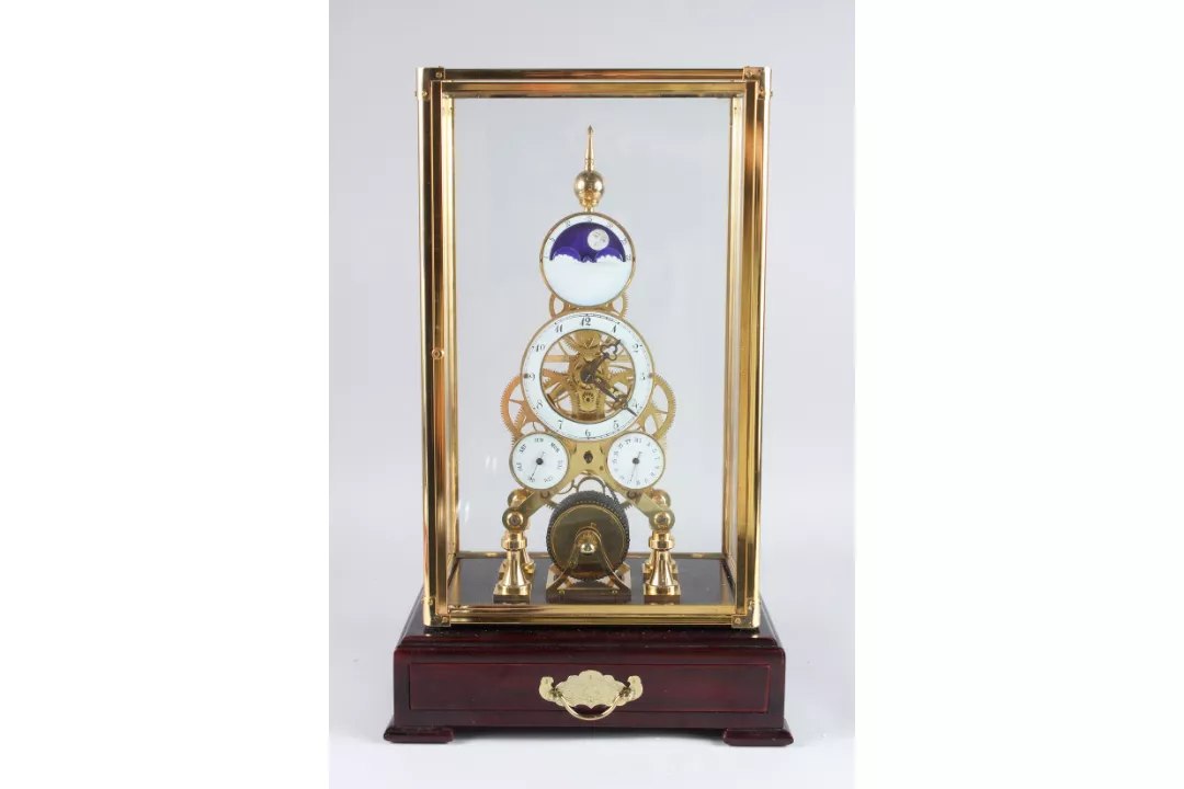 Front view of reproduction brass skeleton clock with moonphase movement inside glazed display case