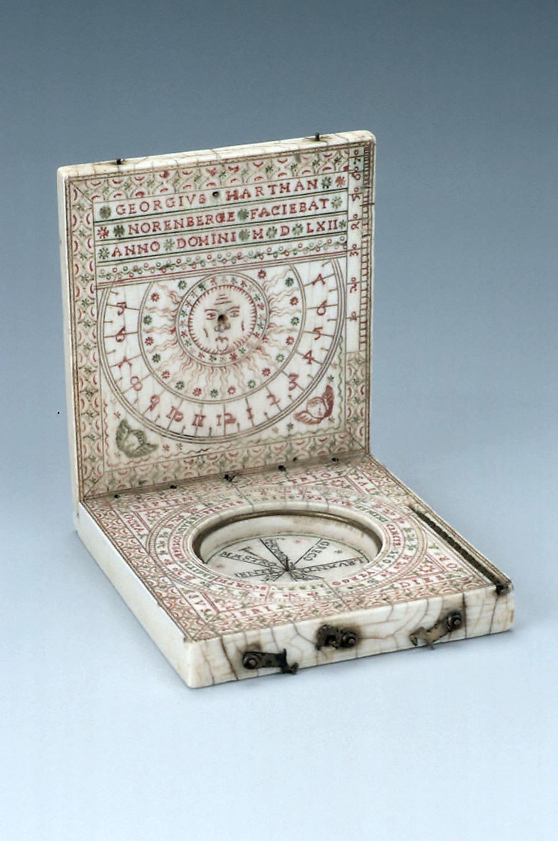 View of the open ivory diptych sundial, showing the interior upper leaf with sun effigy and the lower leaf with an empty compass well.