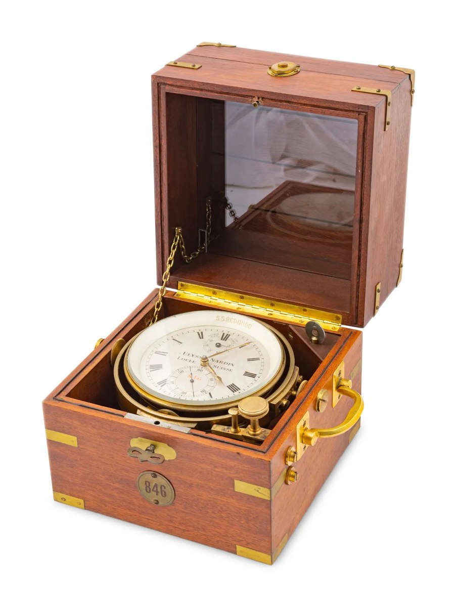Three-quarter view of the Ulysse Nardin marine chronometer in an open wooden box with gimbal mount