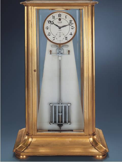 Front view of the gilt bronze mantle regulator featuring a white pyramidal stand and a visible pendulum.