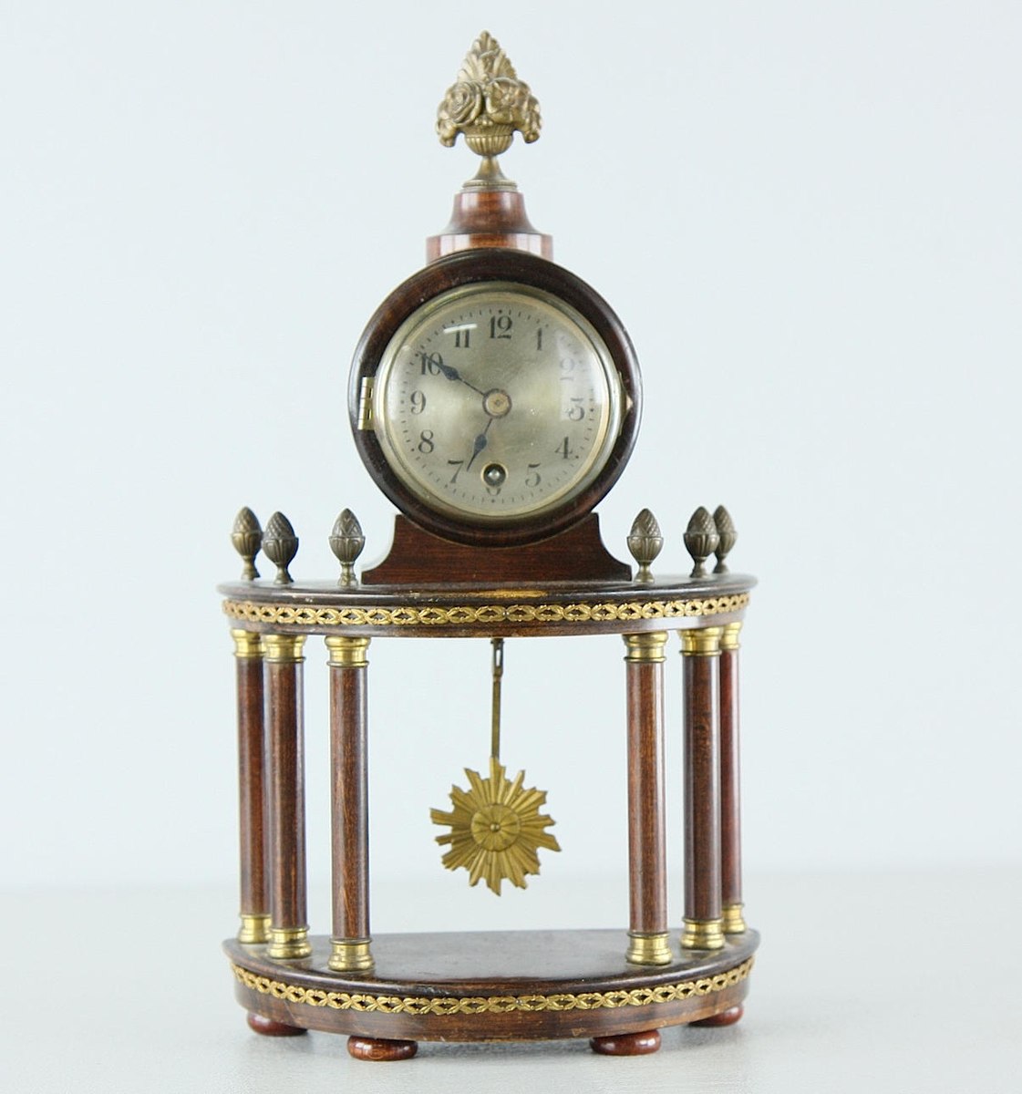 Empire-style portico table clock with six columns, floral crown finial, and sunburst pendulum