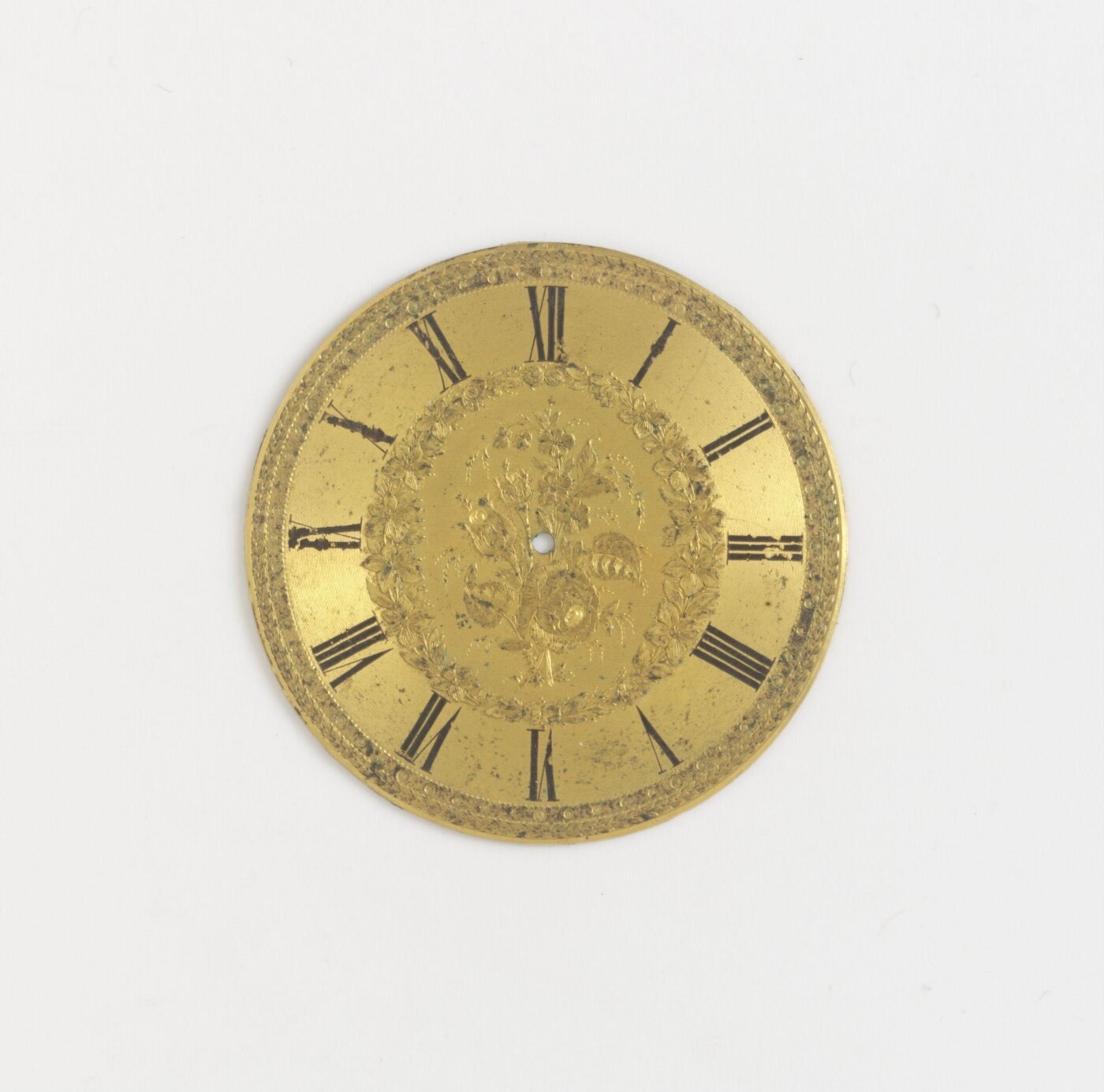 Front view of the gilt metal watch dial showing the engraved floral motifs and painted Roman numerals.