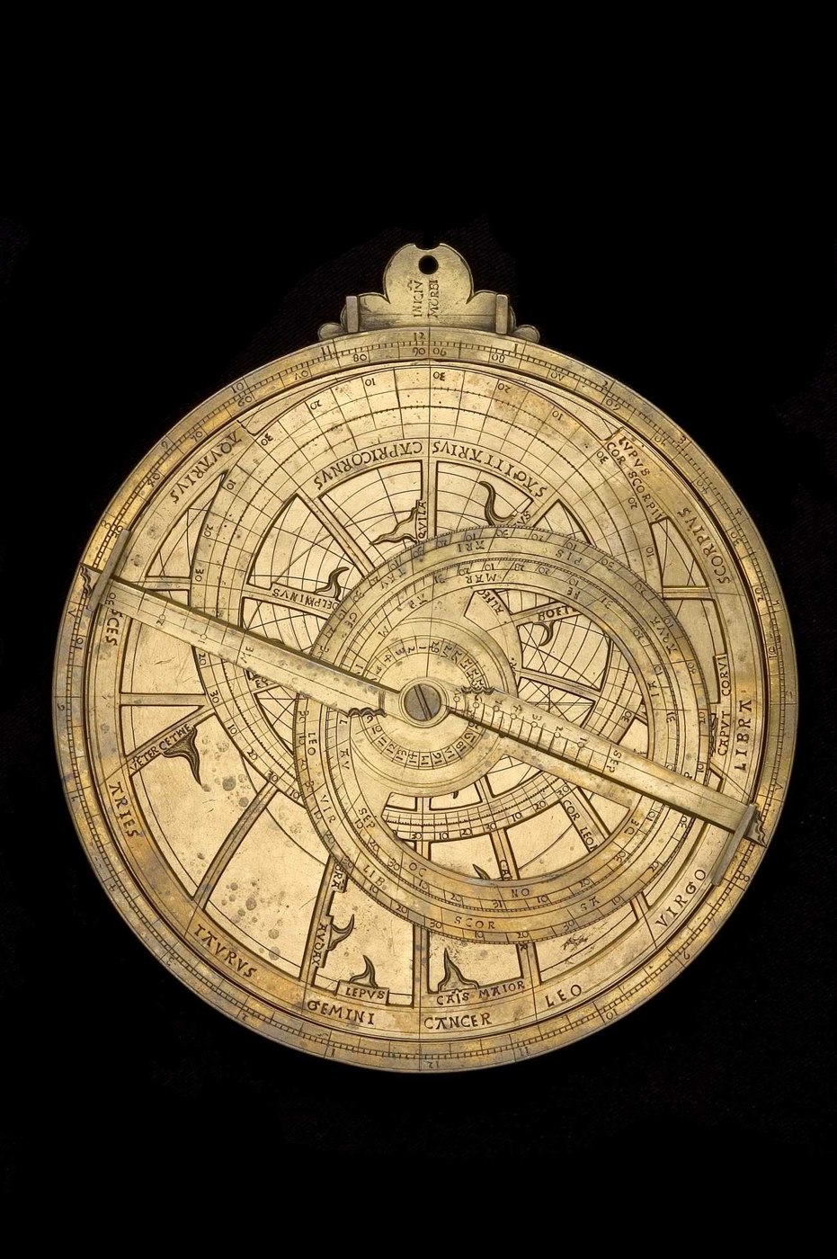 Front view of the brass astrolabe showing the rete, zodiacal markings, and the five-lobed throne at the top.