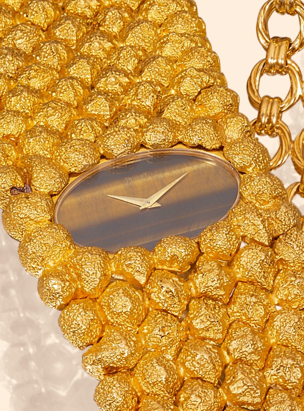 Close-up detail of the 18K yellow gold nugget-textured bracelet and the tiger's eye dial aperture.