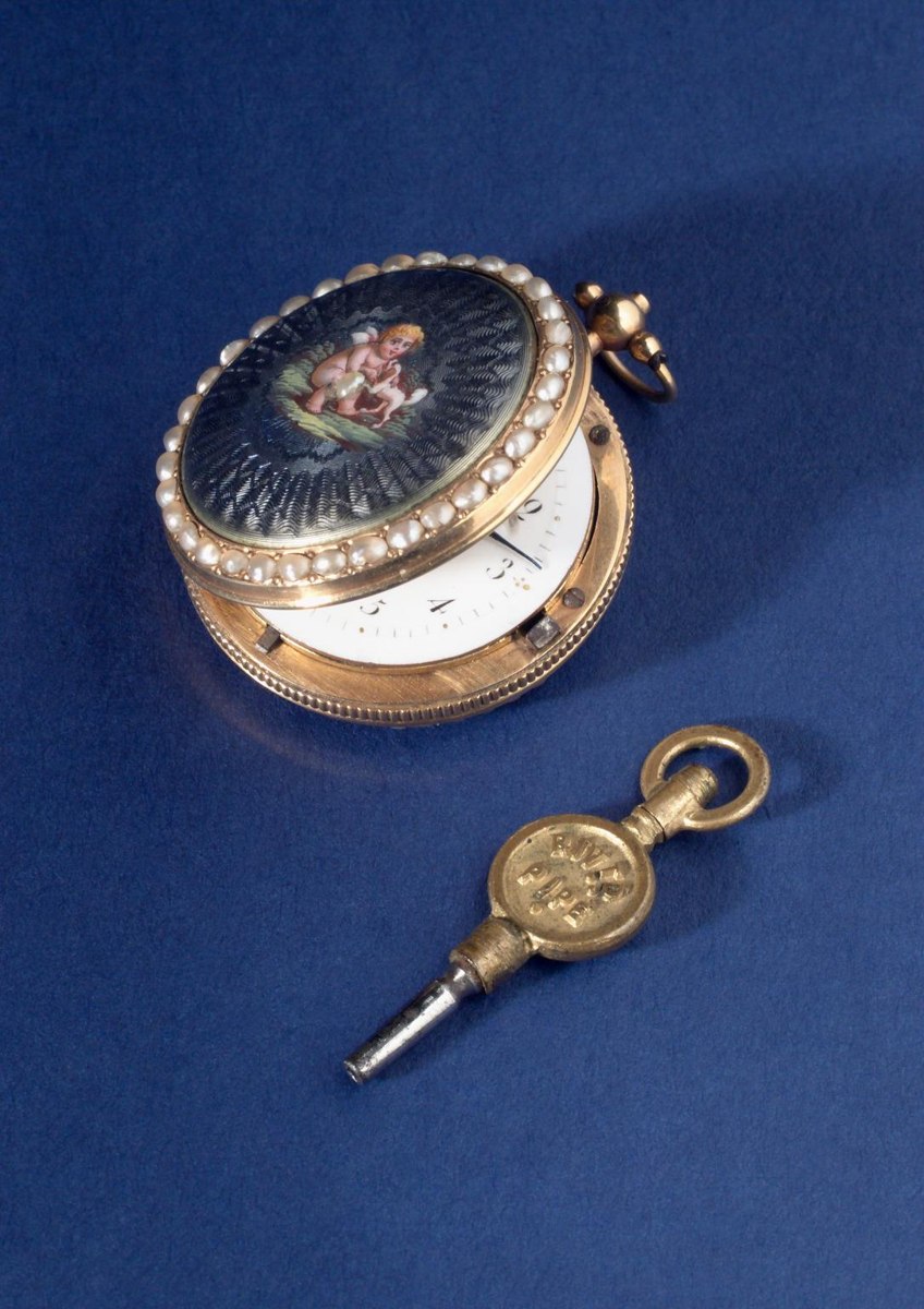 Oblique view of the gold verge hunter pocket watch with enamelled pearl-set lid partially opened, shown with a watch key