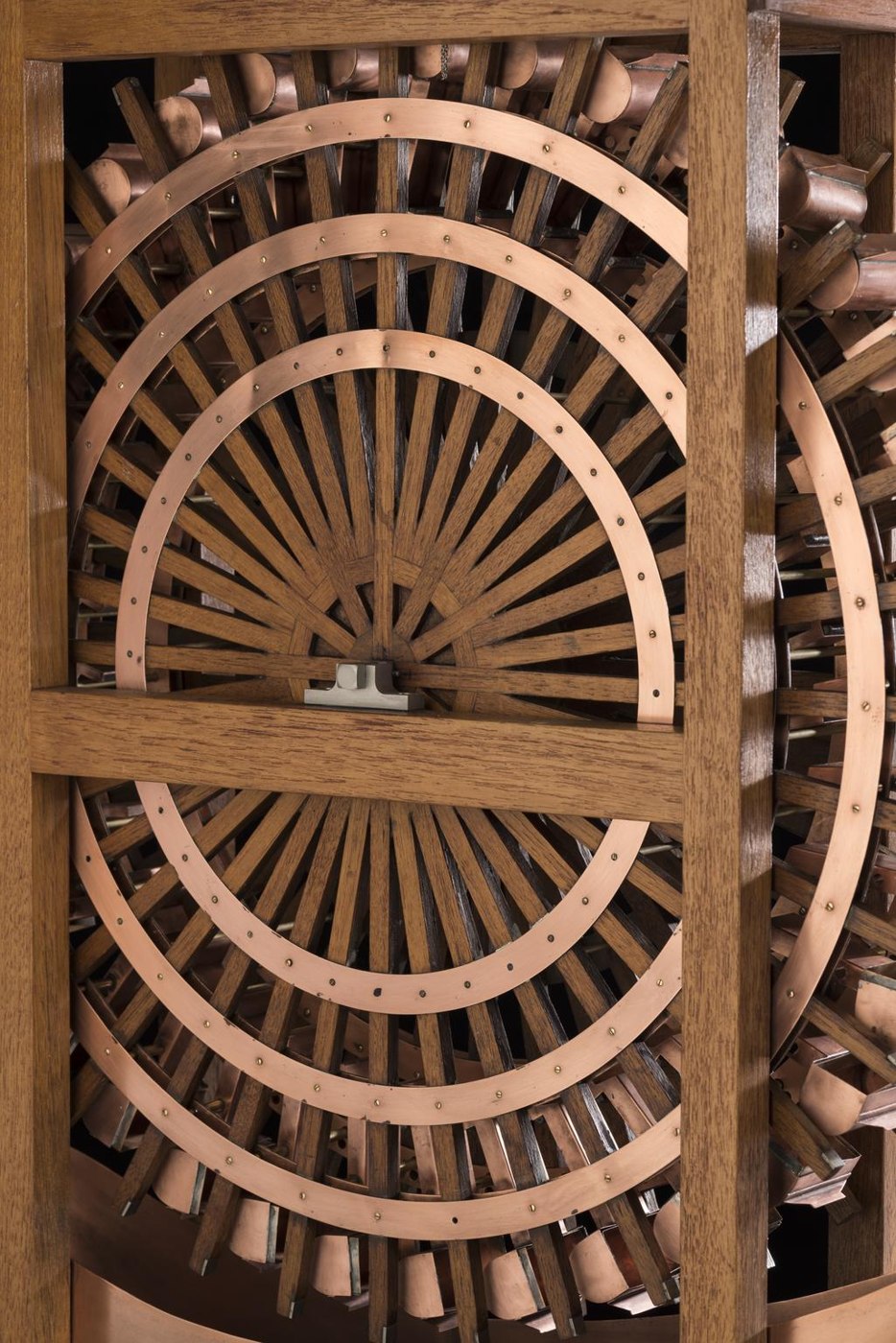 A detailed view of the water-balance wheel assembly, featuring the wooden frame construction, central spoked wheel, and copper buckets.