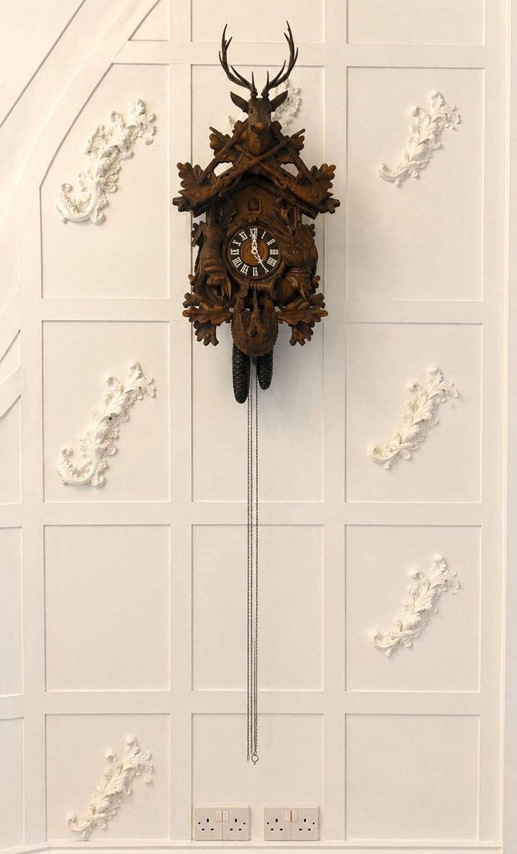 Front view of the Black Forest carved walnut cuckoo clock with suspended weights and chains